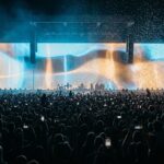 Mulțime la un concert pe stadion, cu un ecran video uriaș strălucind deasupra scenei