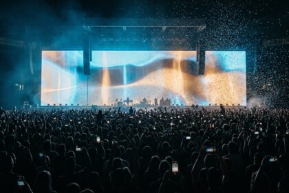 Publikhav på en konsert med en jättelik videoskärm som lyser ovanför scenen
