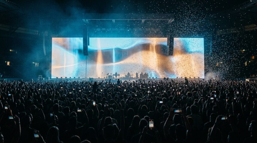 Folla di uno stadio a un concerto con un enorme schermo video che brilla sopra il palco